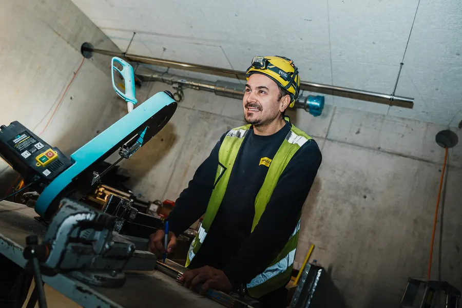 Lachender Monteur mit Helm und Weste an einer Trennmaschine