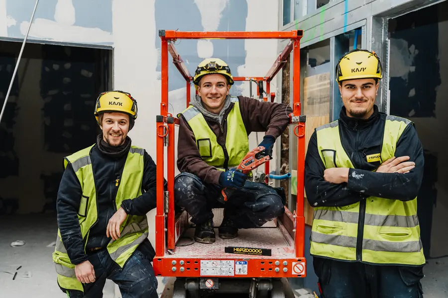 Drei junge Monteure mit Helm posieren an einer Hebebühne
