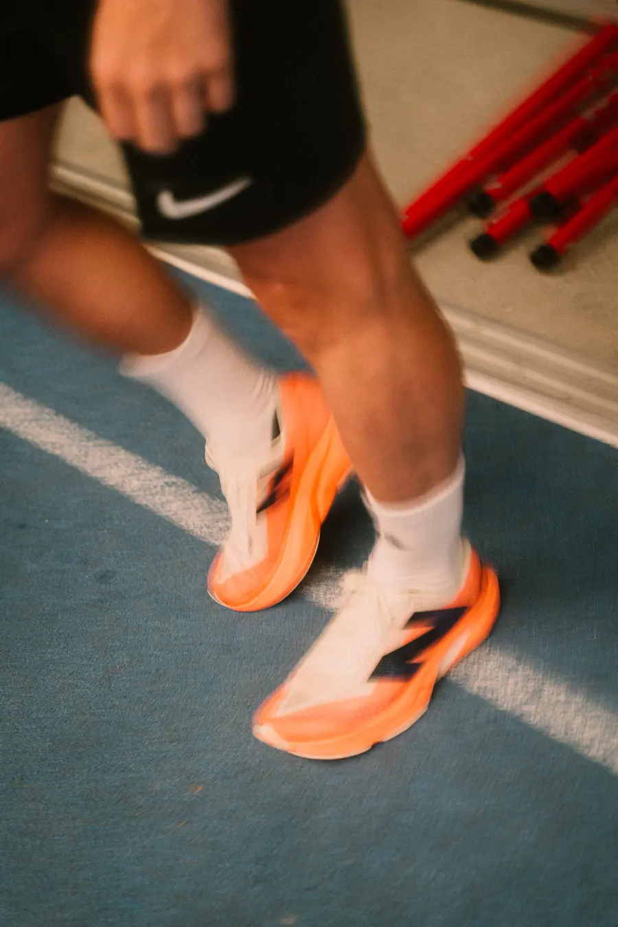 Nahaufnahme orangefarbener Laufschuhe auf der blauen Indoorbahn