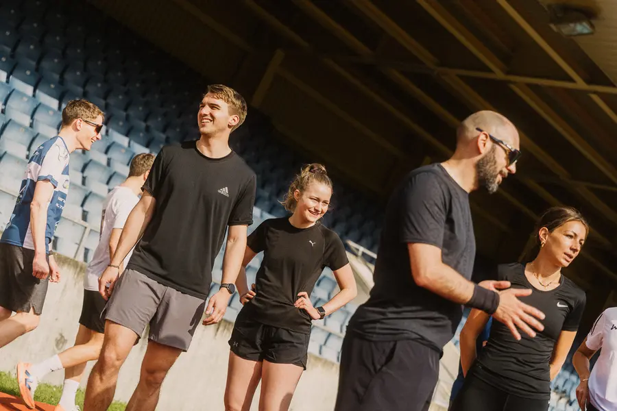 Teilnehmende lachen gemeinsam im Schatten der Tribüne