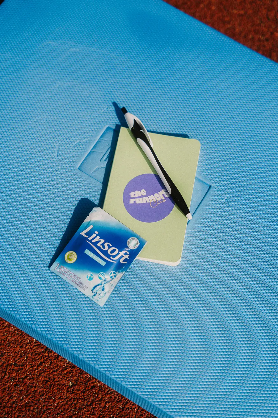 Notizbuch mit The Runners Club Sticker und Stift auf blauer Matte