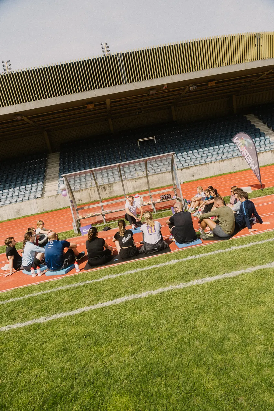 Gruppe sitzt im Kreis auf der Bahn vor der grossen Tribüne