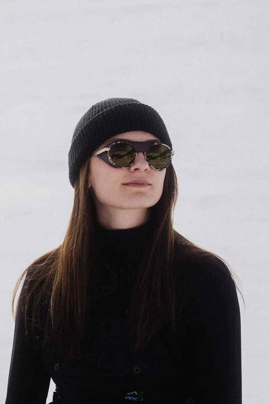 Porträt einer Frau mit runder dunkler Sonnenbrille vor weissem Schnee