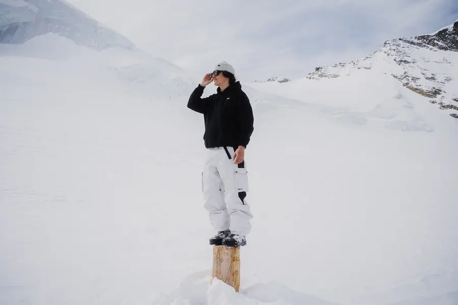 Junger Mann steht auf einem Holzpfosten im weiten Schneefeld