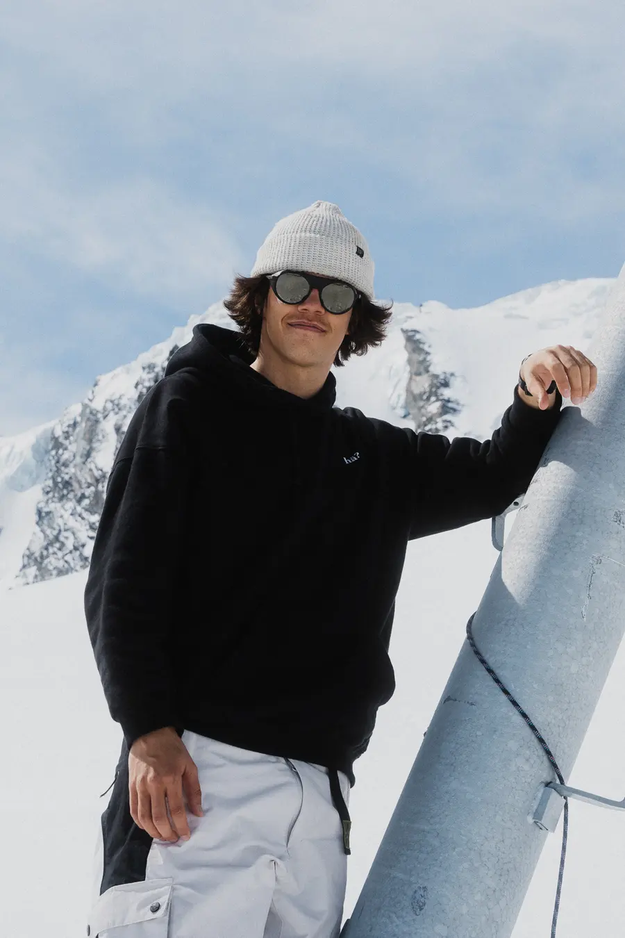 Junger Mann lehnt an einem Skiliftmast unter blauem Himmel