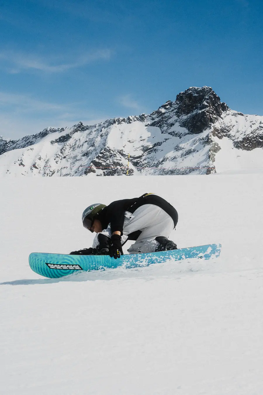 Snowboarder kauert auf einem türkisfarbenen Brett im Neuschnee