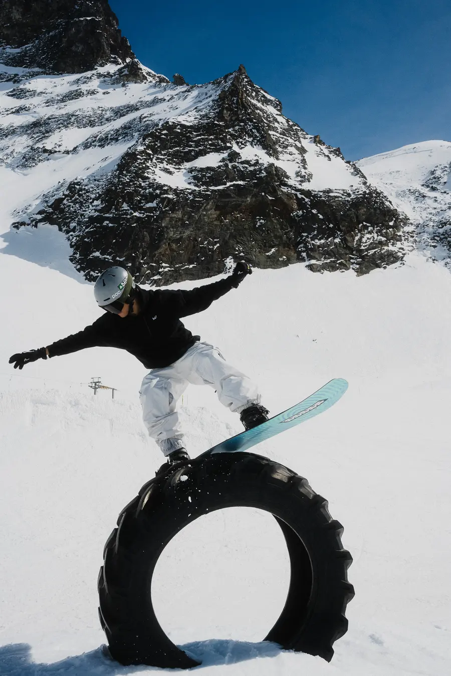 Snowboarder balanciert auf einem Traktorreifen vor felsigen Gipfeln