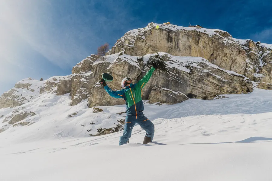 Skifahrer streckt sich im Tiefschnee unter den Felsen nach dem Ball