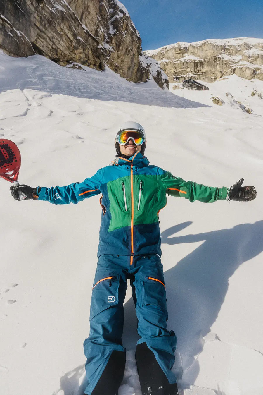 Skifahrer mit ausgebreiteten Armen und Padelschläger im Schnee