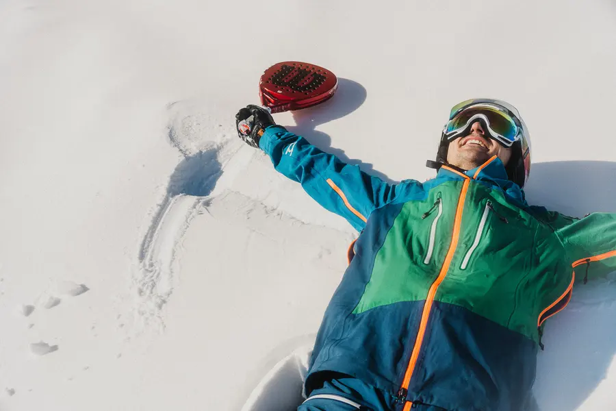 Skifahrer macht mit Padelschläger in der Hand einen Schneeengel