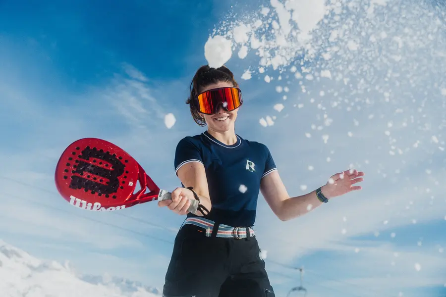 Frau im Sportshirt mit Skibrille spielt Padel im fliegenden Schnee