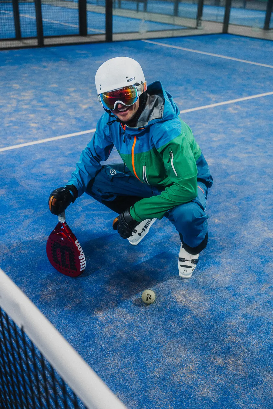 Skifahrer kauert auf dem blauen Platz neben einem Padelball