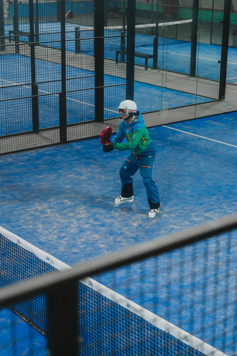 Skifahrer in Spielposition auf dem Padelplatz, über das Netz gesehen
