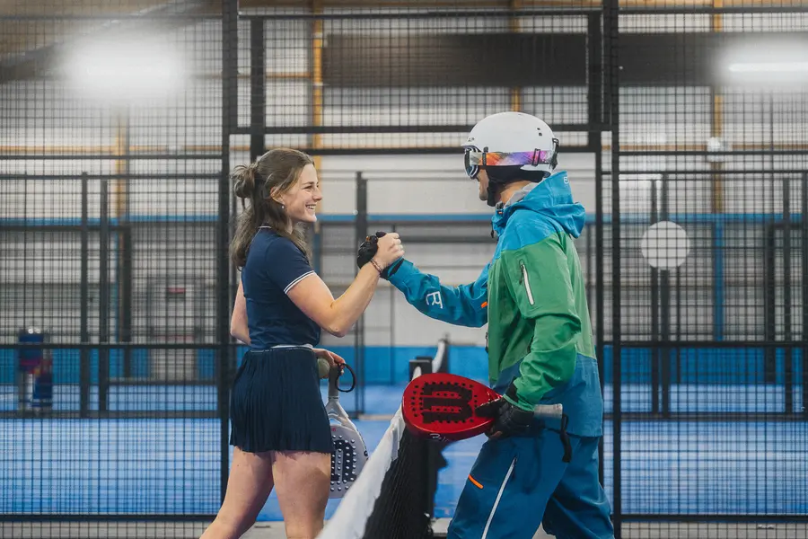 Padelspielerin und Skifahrer reichen sich am Netz die Hand