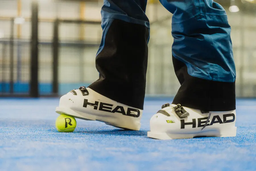 Weisse Skischuhe neben einem Padelball auf dem blauen Platz