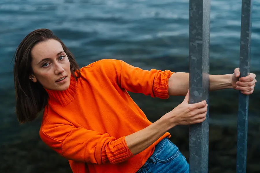 Porträt im orangen Pullover, zwischen Geländerstangen hinausgelehnt