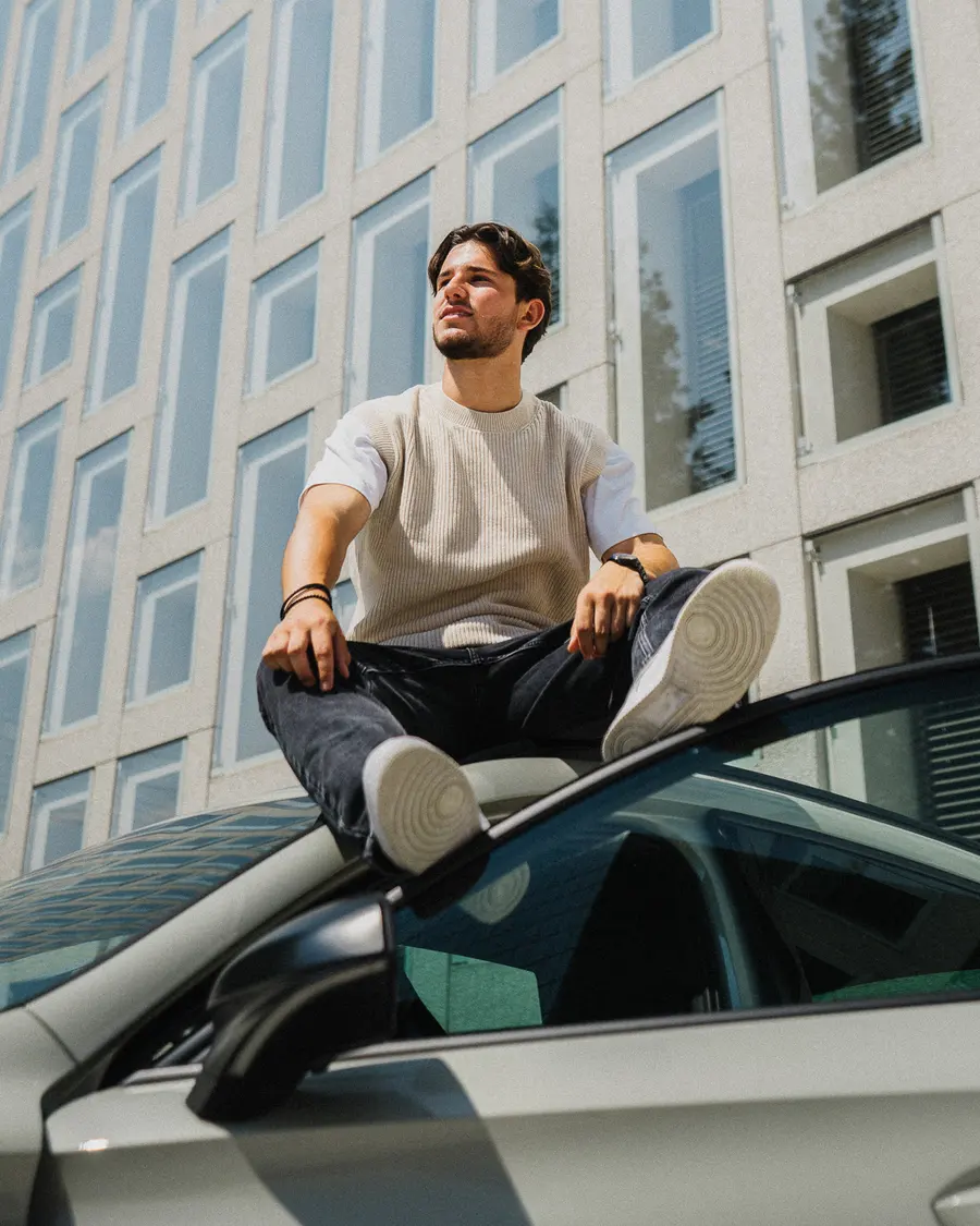 Homme assis sur le toit de la voiture devant une façade quadrillée