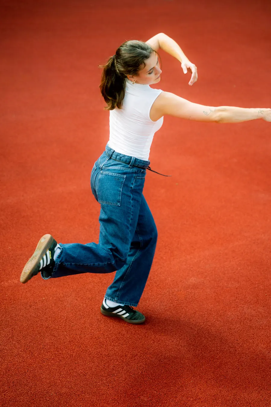 Danseuse sur une jambe, bras arrondis, sur un sol rouge