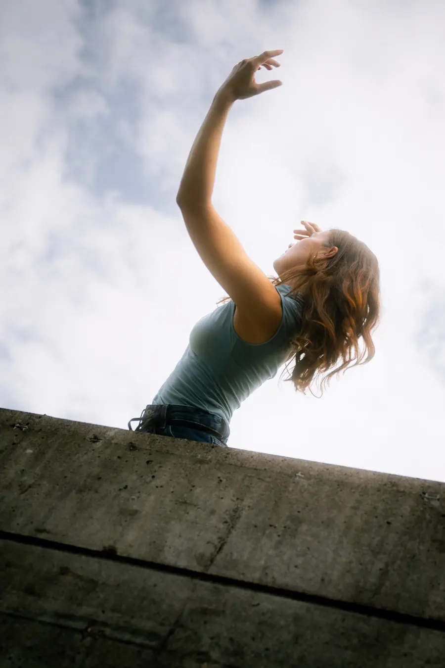 Danseuse tendant la main vers le ciel au-dessus d’un mur de béton