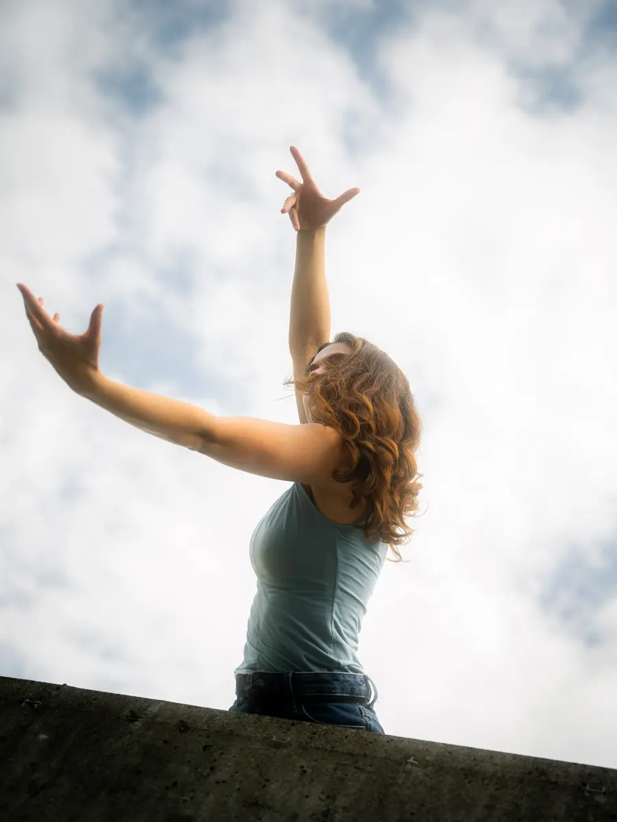 Danseuse vue d’en bas, bras levés devant un ciel nuageux