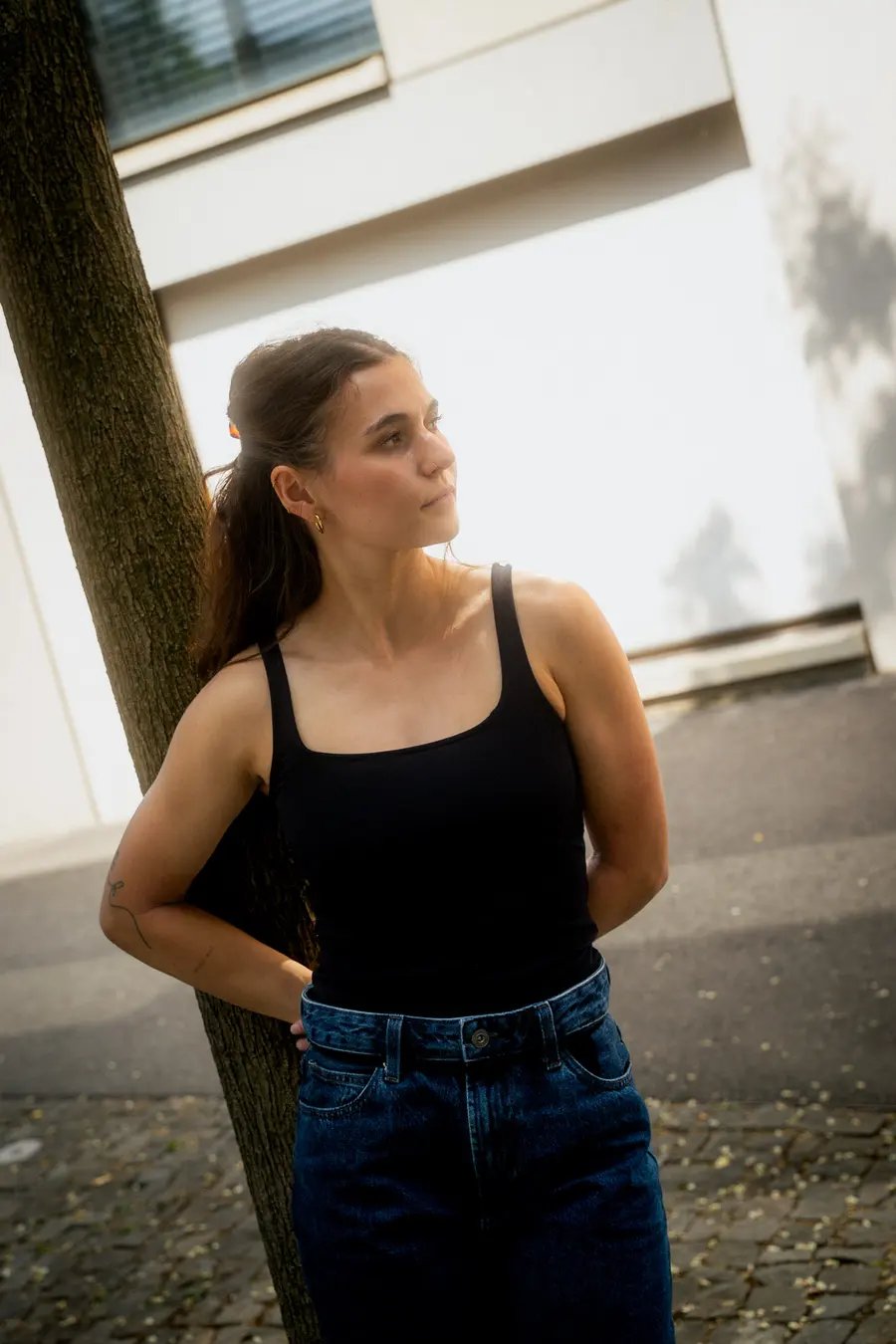 Portrait calme en haut noir contre un arbre et un mur clair