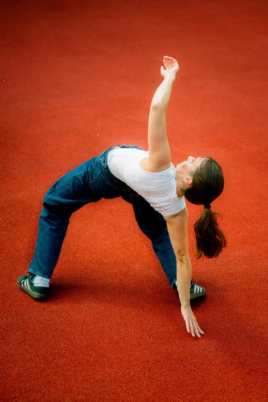 Danseuse en profonde flexion latérale, bras levé, sur sol rouge