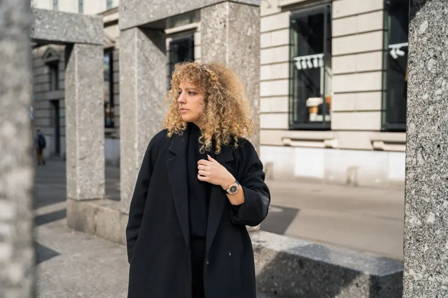 Femme en long manteau noir entre des colonnes de pierre