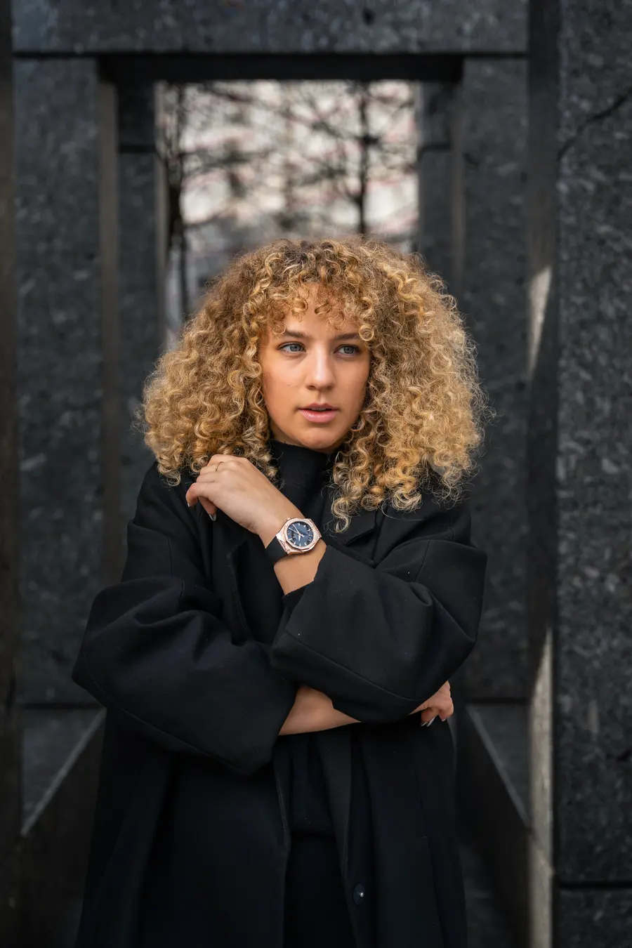 Femme aux cheveux bouclés montrant sa montre entre des colonnes de granit