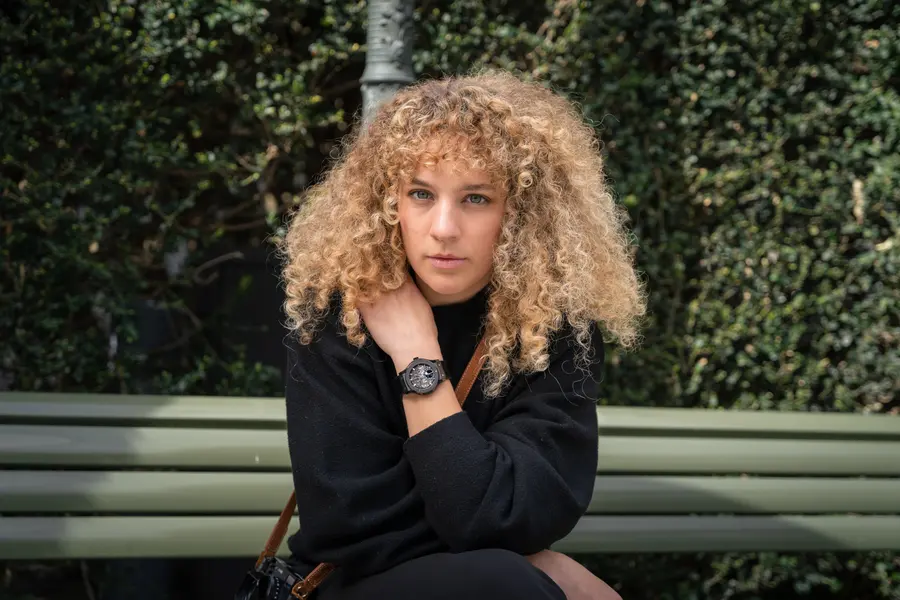 Femme aux cheveux bouclés sur un banc, la montre près du col