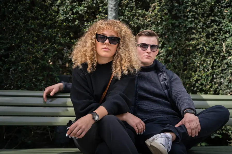 Couple à lunettes de soleil assis sur un banc devant du lierre