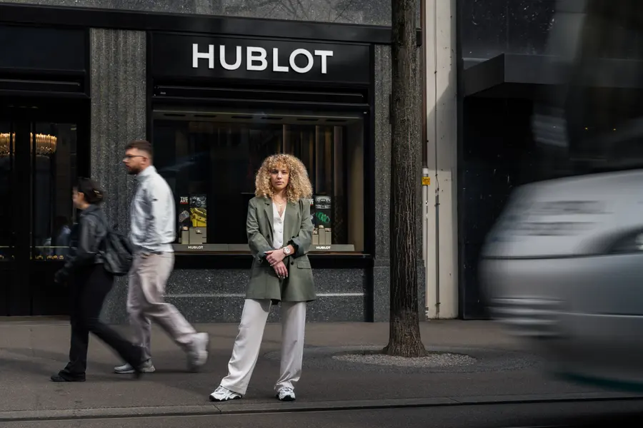 Femme en blazer vert devant la boutique Hublot, passants autour