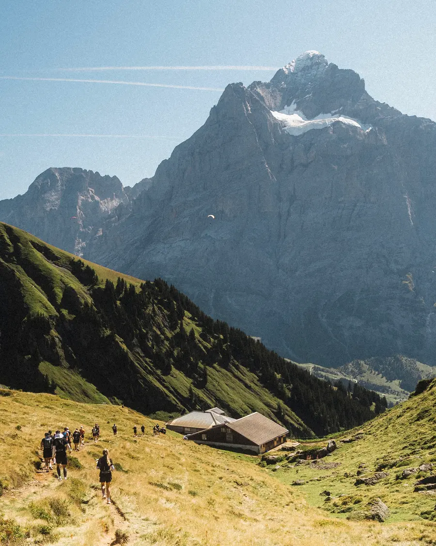 Eine Reihe Läufer zieht Richtung Alphütte unter einem mächtigen Gipfel