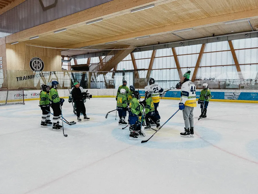 Eishockeytraining in einem Trainingszentrum: junge Spieler in grünen Trikots, mitten unter ihnen die Kamera auf dem Eis