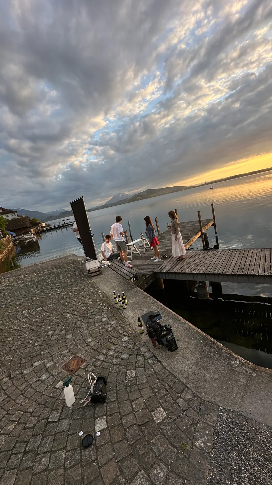 Abend am Steg: Das Team richtet sich bei Sonnenuntergang ein, Flaschen und Kamera stehen auf dem Steinquai