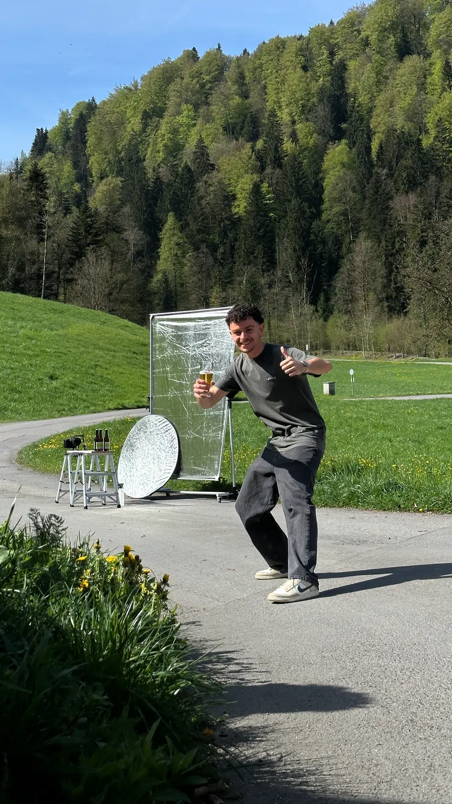 Aussendreh: Jemand aus dem Team zeigt mit einem Glas Bier den Daumen hoch, dahinter Reflektor und Diffusor