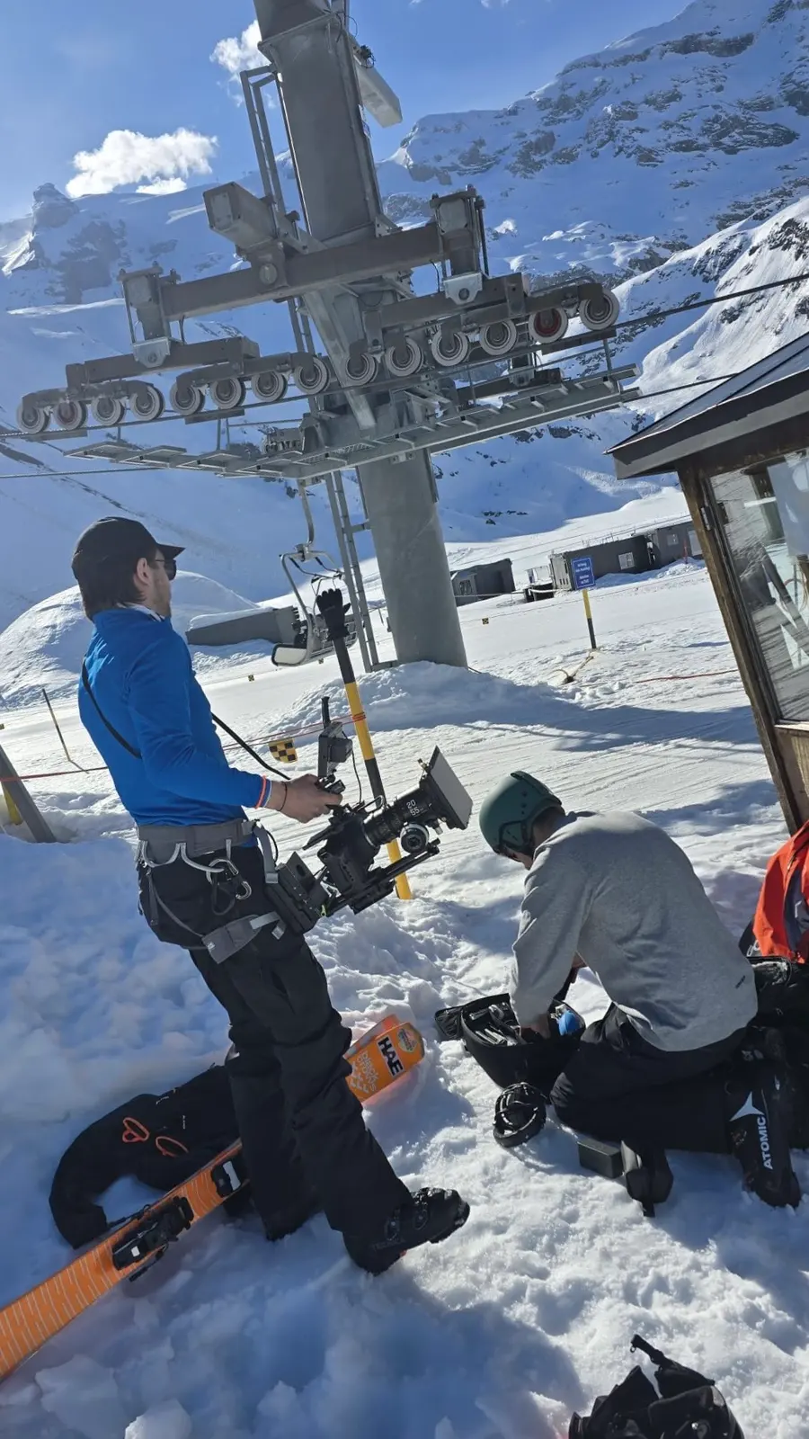 Dreh im Schnee bei einem Sessellift: Kamera am Gimbal, daneben packt jemand aus dem Team Material neben einem Snowboard aus