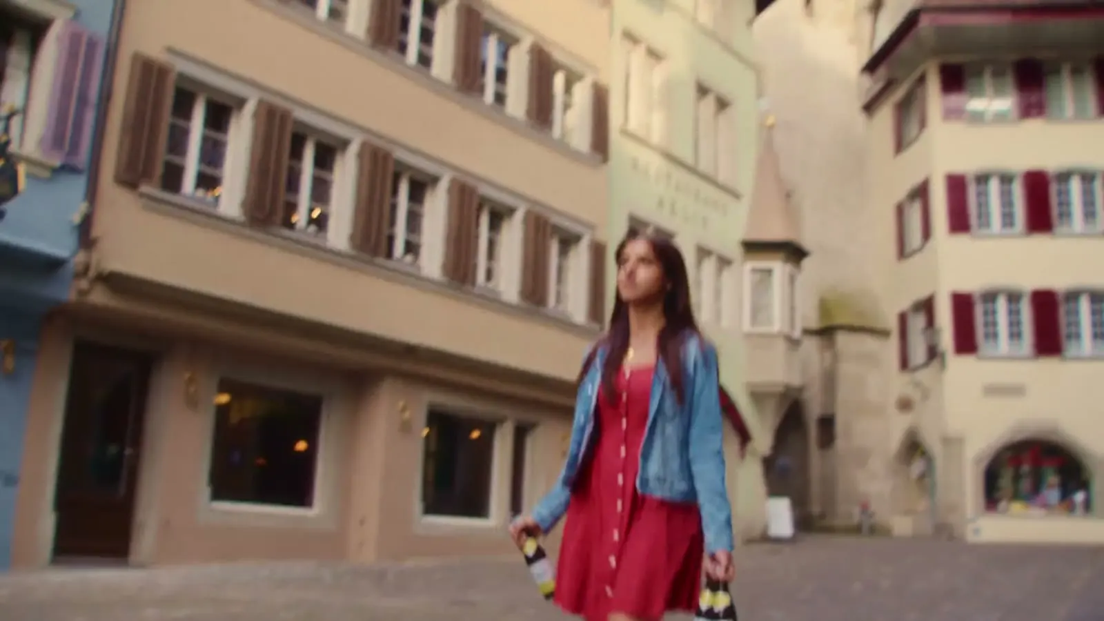 Junge Frau im roten Kleid geht mit Panasch-Flaschen durch eine Altstadtgasse