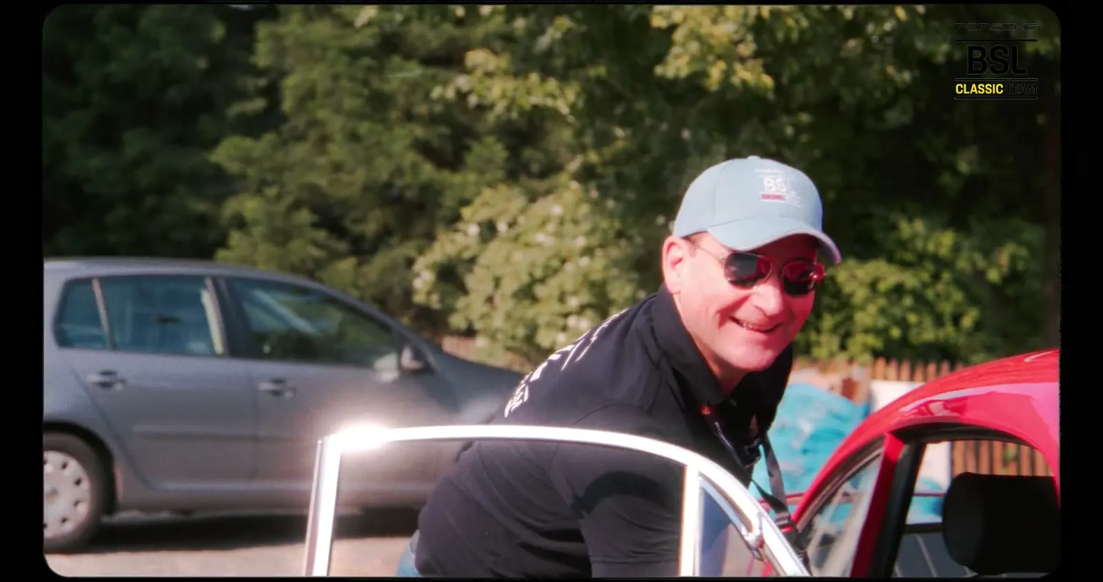Conducteur souriant en casquette près de la portière ouverte d’une Porsche 911 rouge
