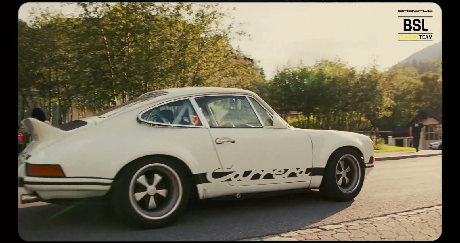 Porsche 911 Carrera RS blanche avec lettrage latéral sur une route de village