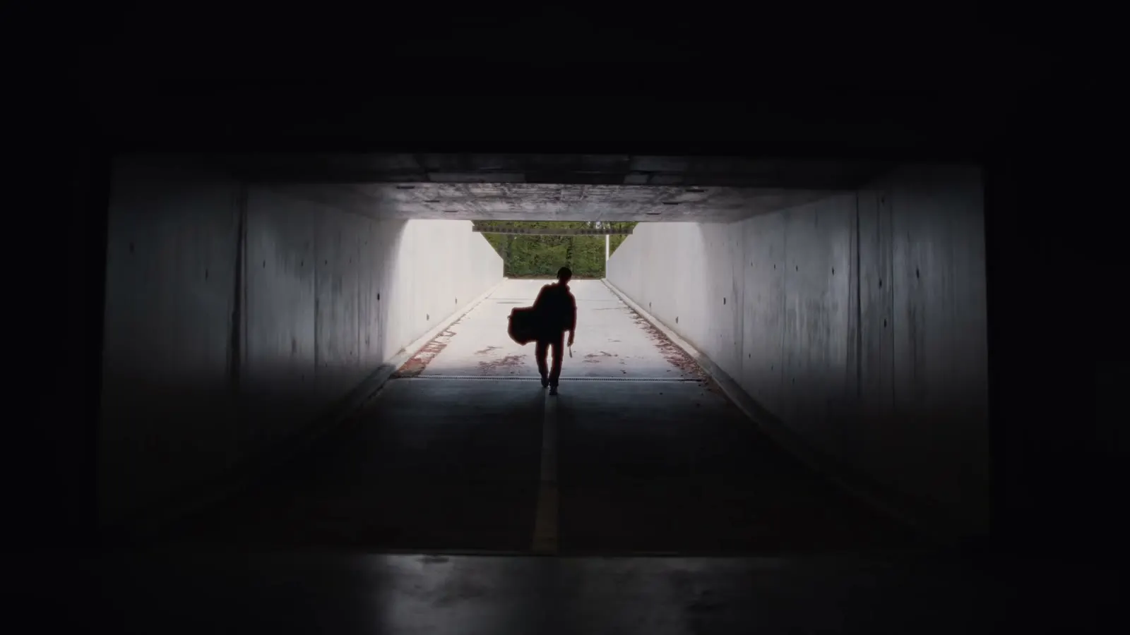 Silhouette eines Spielers mit Tasche in einem dunklen Betontunnel