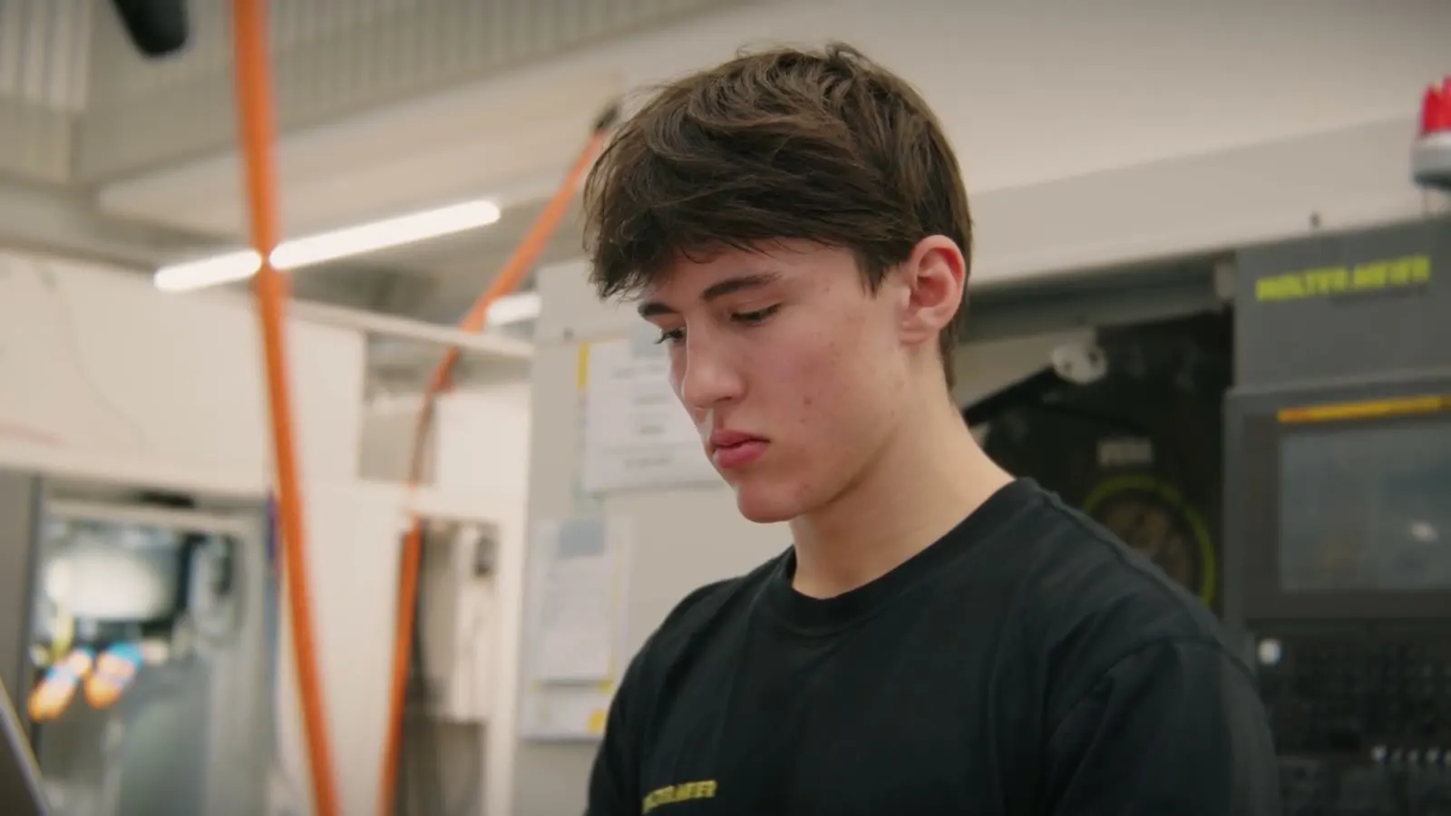 Junger Mann im schwarzen Walter-Meier-T-Shirt konzentriert an einer Maschine