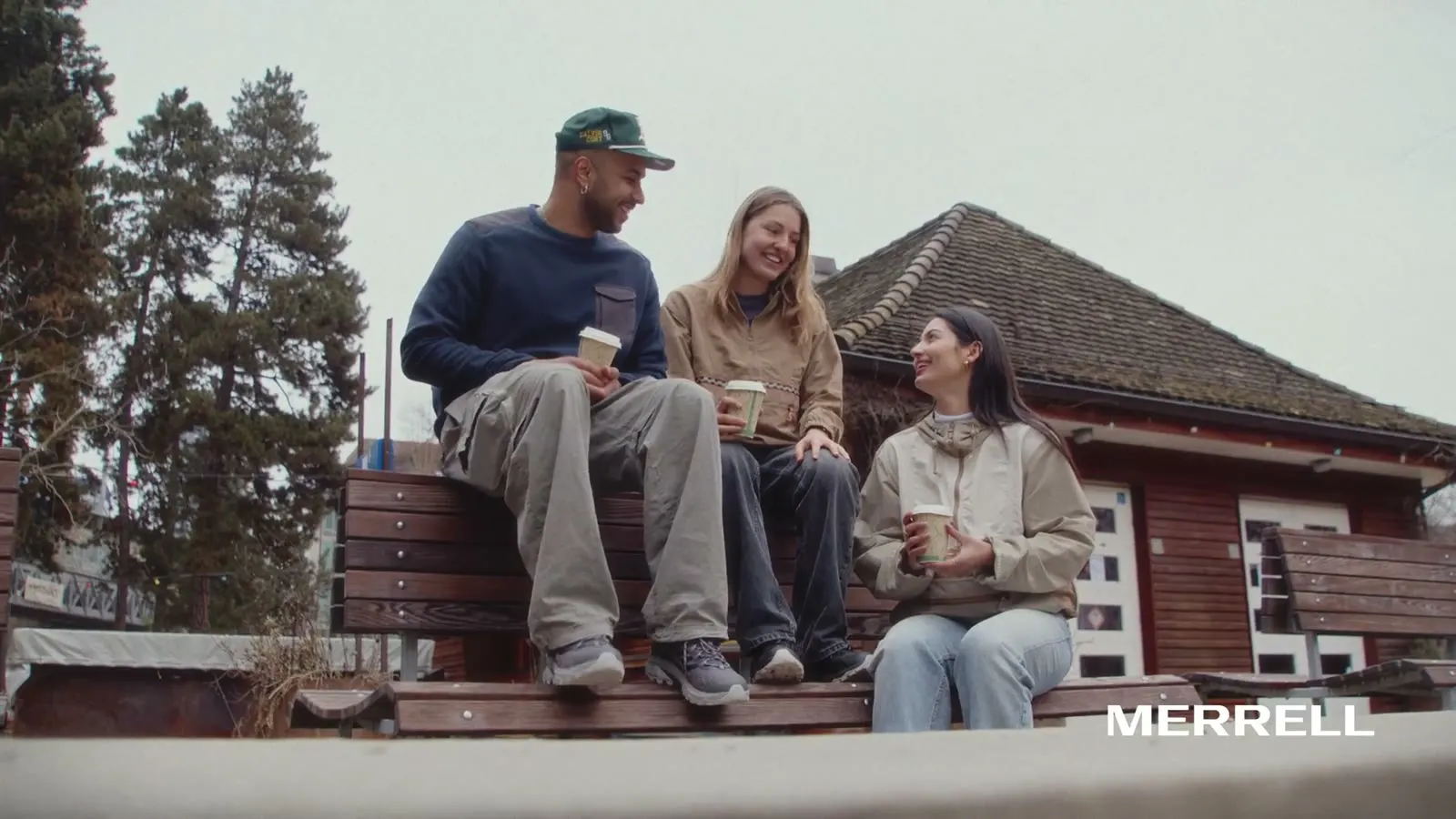 Drei Freunde mit Kaffeebechern auf einer Holzbank vor einem Häuschen