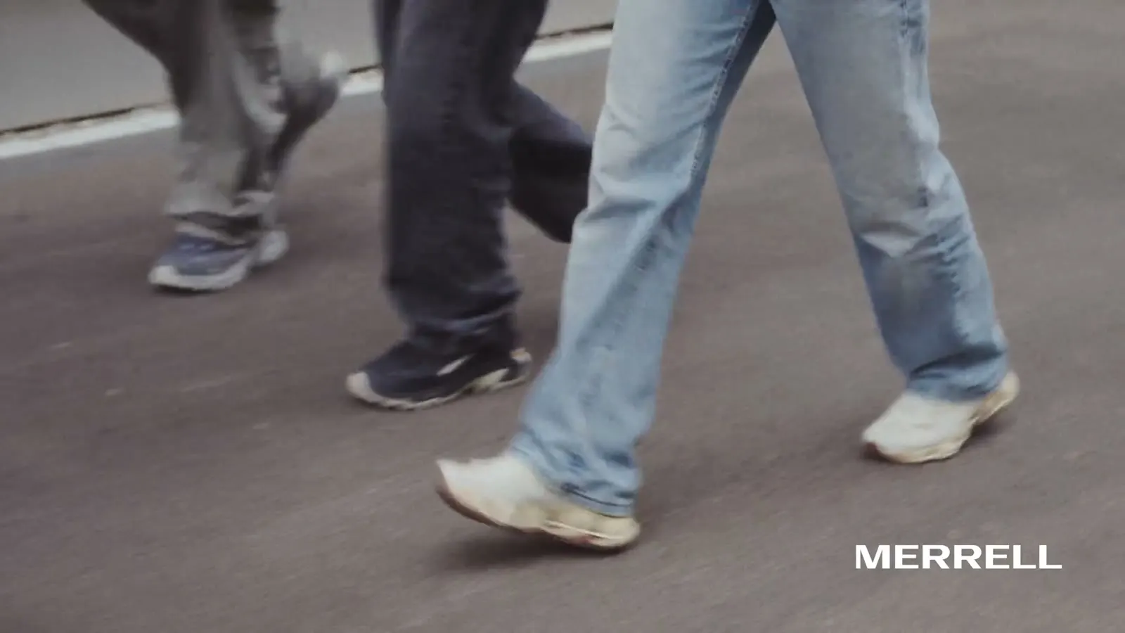 Beine in weiten Jeans und Merrell-Schuhen beim Gehen über Asphalt